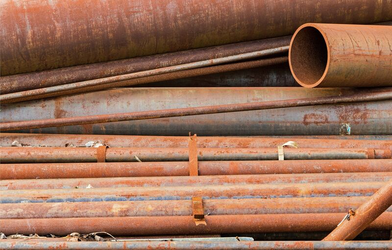 A pile of rusty pipes of many different diameters lying side by side, with the open end of one pipe at the upper right